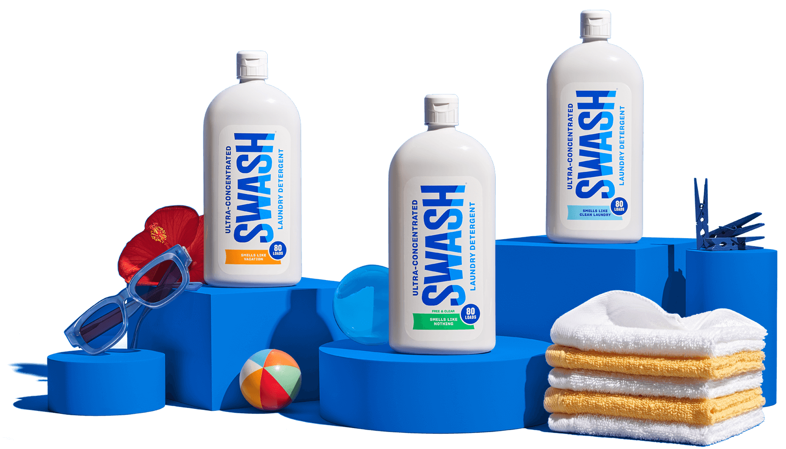 A collection of the three bottles of Swash® Laundry Detergent on pedestals, with different themed items like vacation gear and laundry pins set up around the bottles.