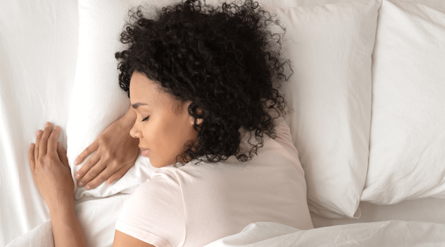 A woman sleeps on clean, white sheets with her head on a fresh pillow.