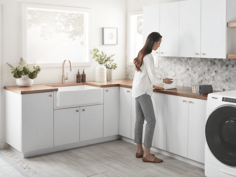 A woman in a white blouse folding her laundry in her laundry room.