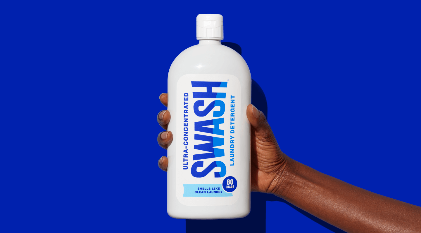 A hand holding a bottle of Swash® Smells Like Clean Laundry